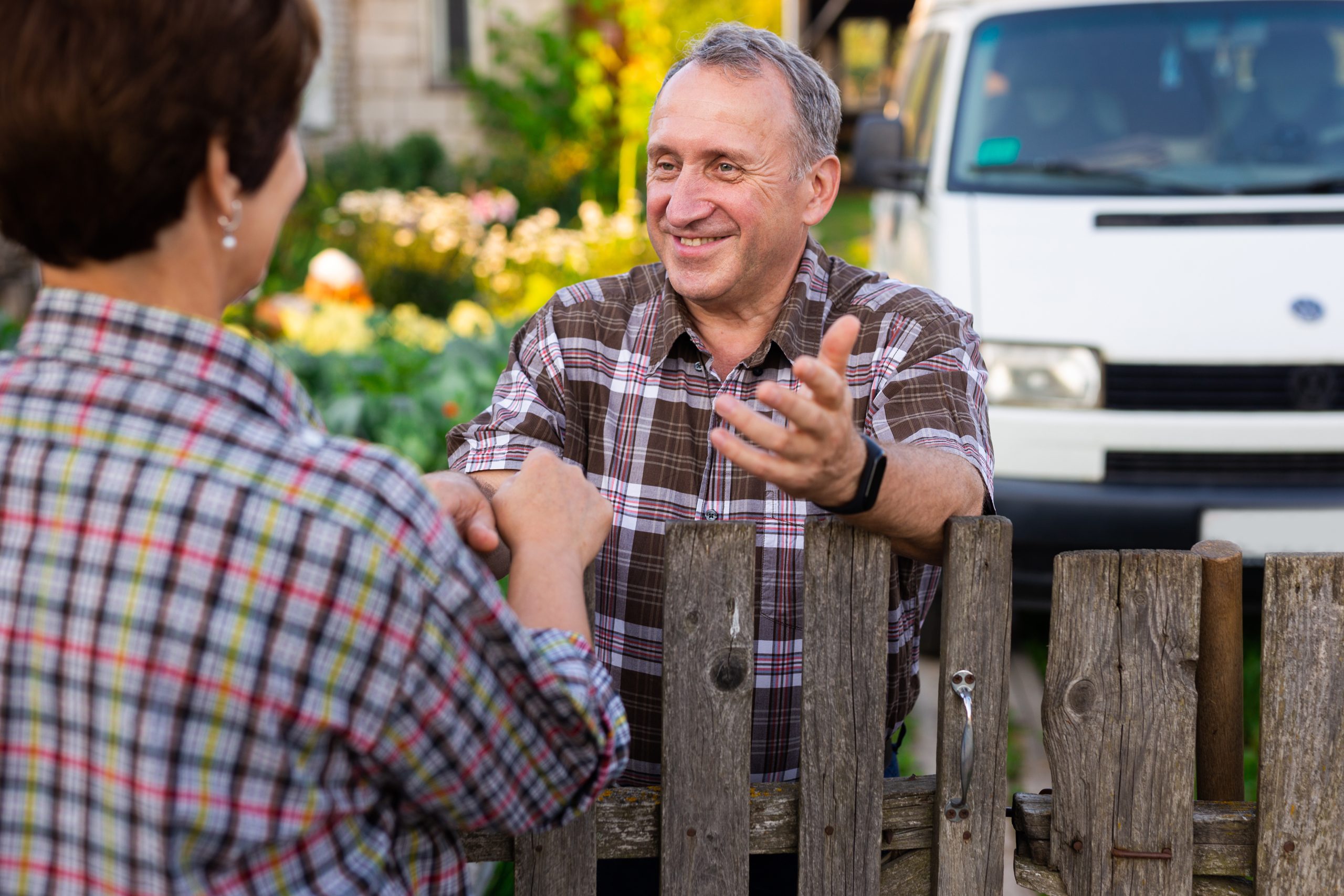 neighbors middle aged man and woman chatting on either side of a fence gate